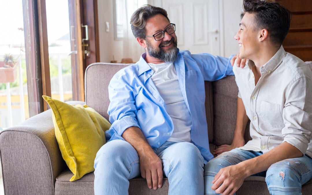 Happy father and son talking while sitting on sofa at home.